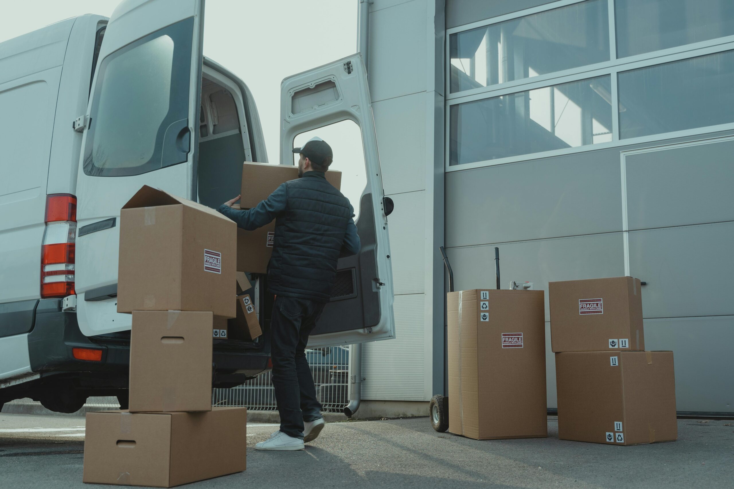 pexels photo 6169056 6169056 A delivery man unloading cardboard boxes from a van at a warehouse during the day.